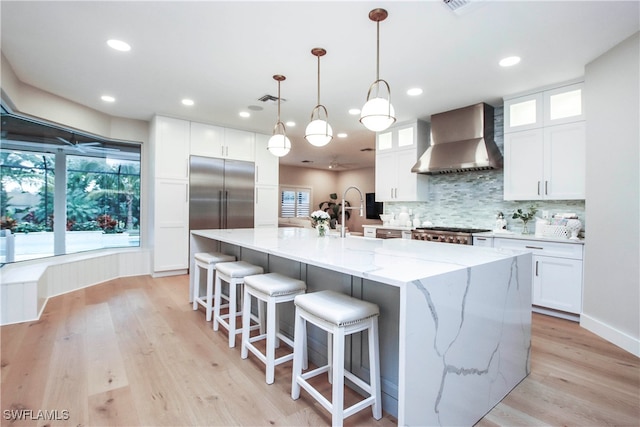 kitchen featuring wall chimney exhaust hood, a kitchen island with sink, and white cabinets