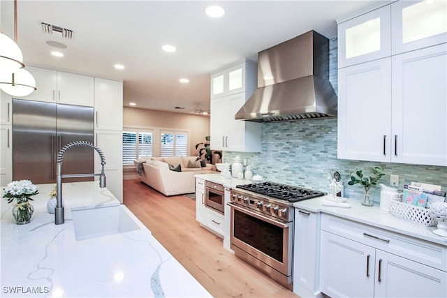 kitchen featuring wall chimney exhaust hood, high end appliances, and white cabinetry