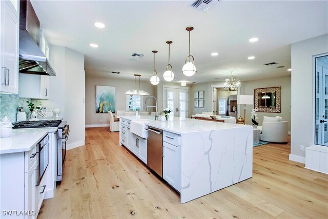 kitchen with a large island, white cabinetry, wall chimney range hood, appliances with stainless steel finishes, and decorative light fixtures