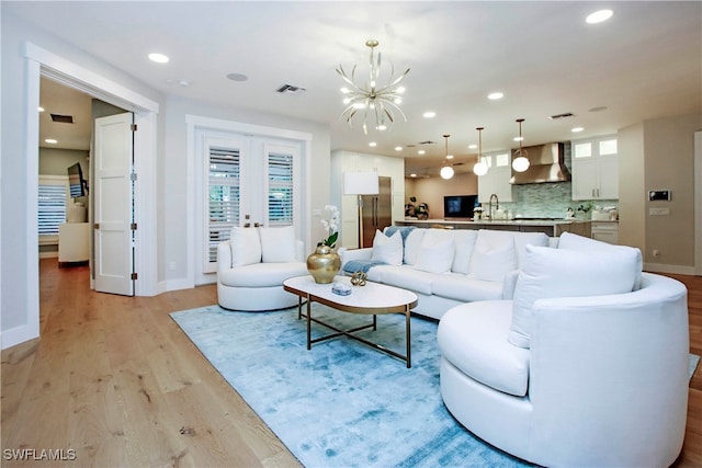 living room featuring light hardwood / wood-style flooring, sink, an inviting chandelier, and french doors