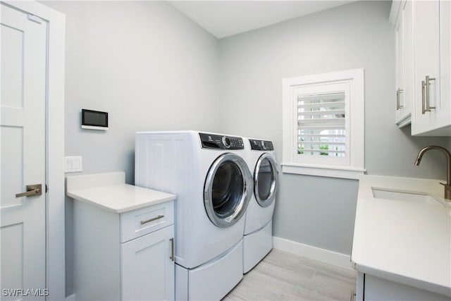 laundry area featuring separate washer and dryer, cabinets, light wood-type flooring, and sink