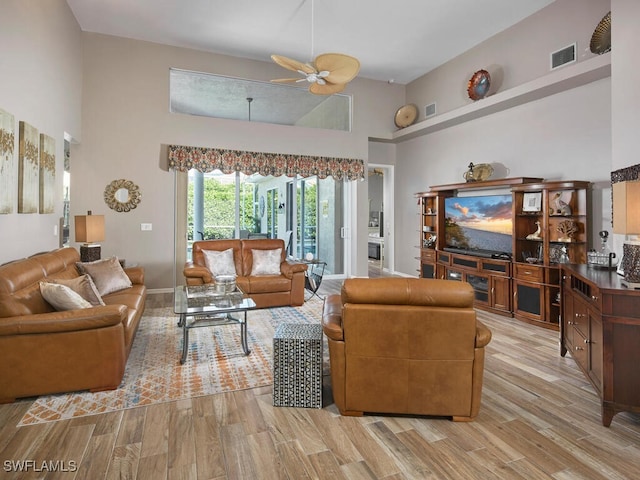 living room with ceiling fan, a towering ceiling, and light hardwood / wood-style flooring