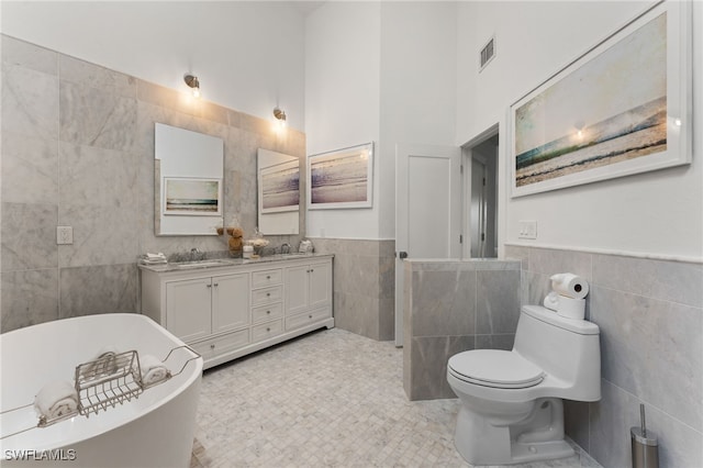 bathroom with double vanity, visible vents, a freestanding bath, tile walls, and a sink
