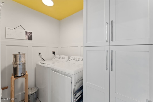 laundry area featuring cabinet space, washer and dryer, wainscoting, and a decorative wall
