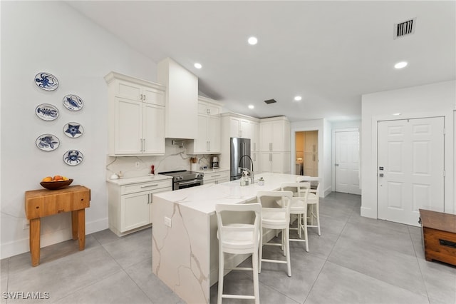 kitchen with white cabinetry, light stone counters, appliances with stainless steel finishes, and a center island with sink