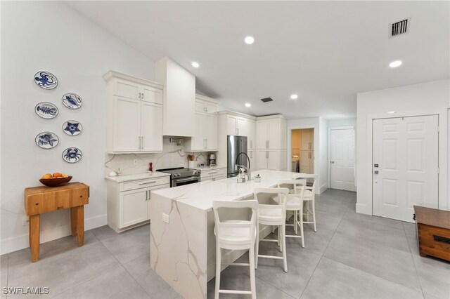 kitchen featuring stainless steel appliances, baseboards, white cabinetry, visible vents, and a center island with sink