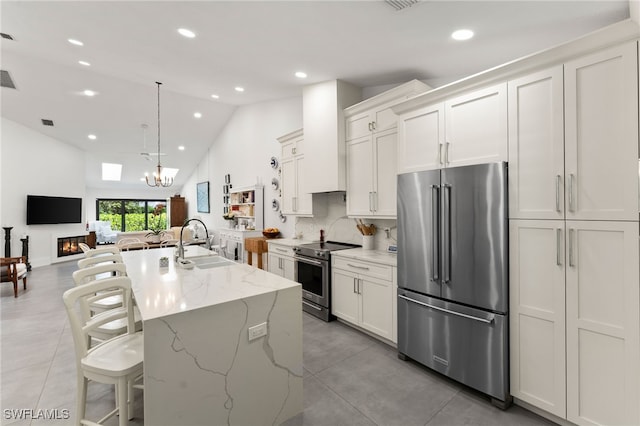 kitchen with appliances with stainless steel finishes, pendant lighting, white cabinets, light stone counters, and a kitchen island with sink