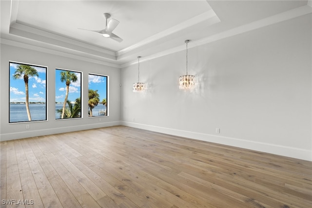 spare room with ceiling fan with notable chandelier, light hardwood / wood-style flooring, a tray ceiling, and a water view