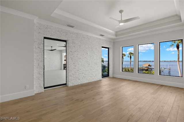 spare room with a water view, ceiling fan, a raised ceiling, and light hardwood / wood-style flooring