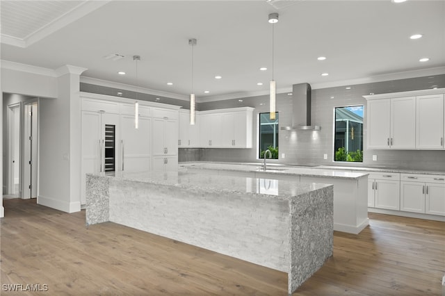 kitchen with light stone countertops, wood-type flooring, a large island, wall chimney exhaust hood, and pendant lighting