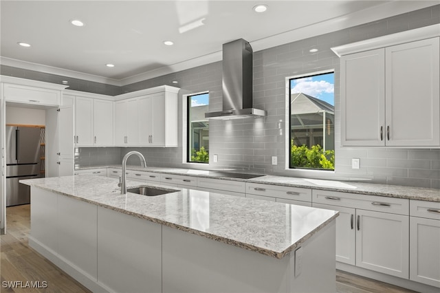 kitchen with sink, stainless steel fridge, wall chimney exhaust hood, white cabinets, and light hardwood / wood-style flooring