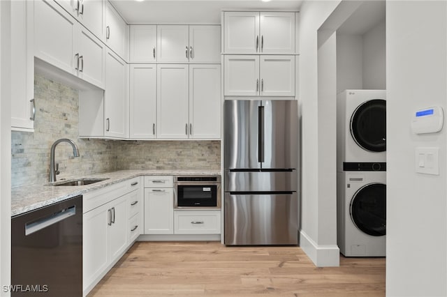 kitchen with appliances with stainless steel finishes, white cabinets, stacked washer and dryer, and sink