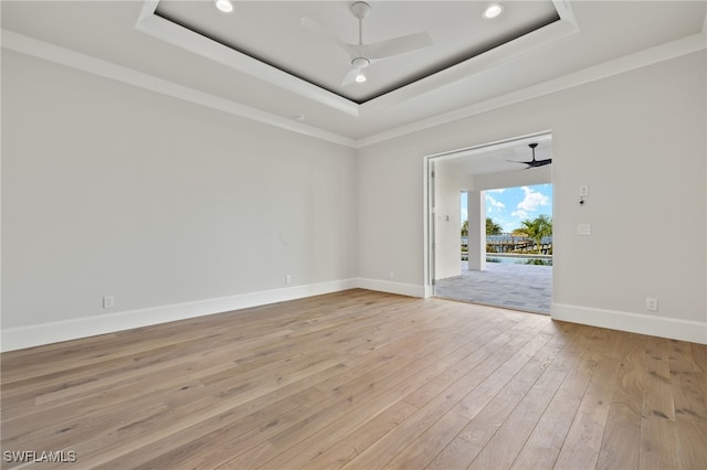 empty room with light hardwood / wood-style floors, crown molding, a tray ceiling, and ceiling fan