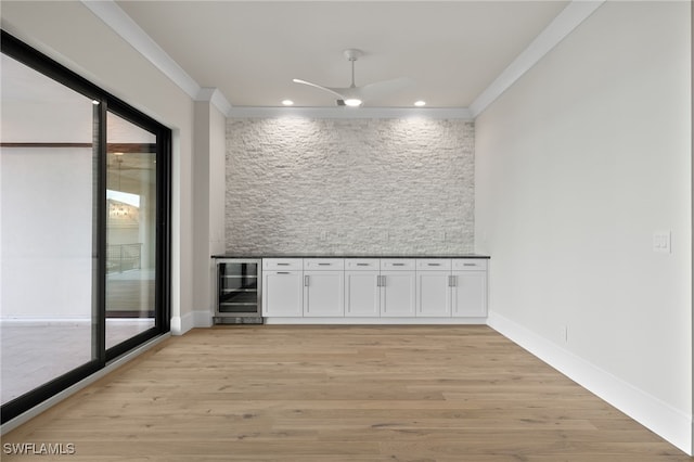 bar featuring beverage cooler, light wood-type flooring, plenty of natural light, white cabinets, and crown molding