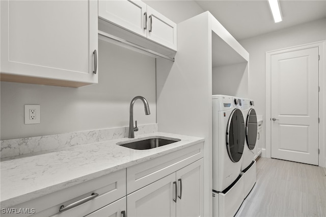 laundry room featuring sink, washer and clothes dryer, light hardwood / wood-style flooring, and cabinets