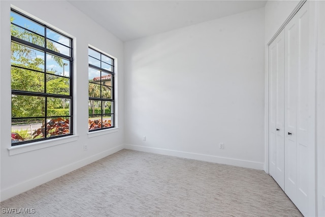 unfurnished bedroom with light colored carpet, multiple windows, and a closet