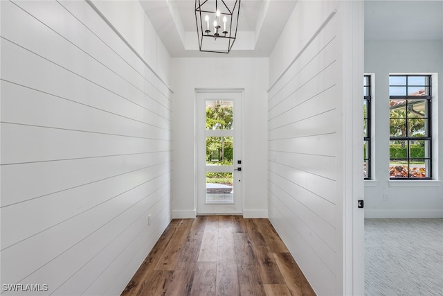 doorway to outside featuring a wealth of natural light, wooden walls, a notable chandelier, and dark hardwood / wood-style floors