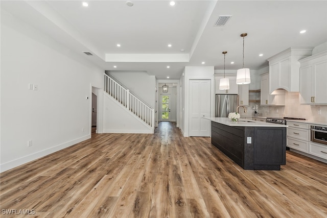 kitchen featuring stainless steel appliances, pendant lighting, an island with sink, white cabinets, and light hardwood / wood-style flooring