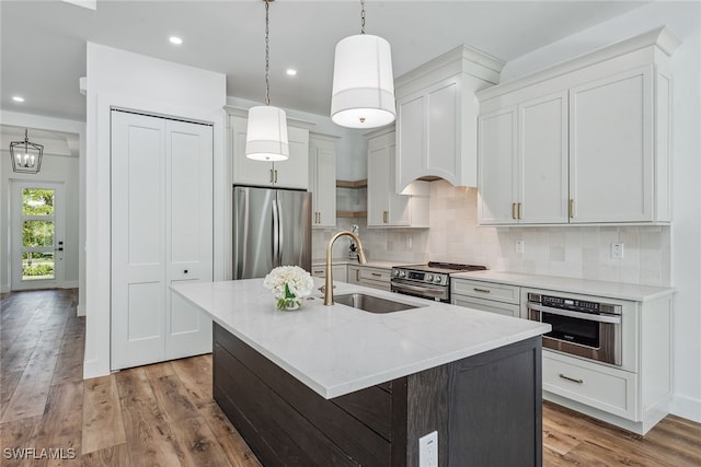 kitchen with white cabinetry, appliances with stainless steel finishes, hanging light fixtures, an island with sink, and light hardwood / wood-style floors