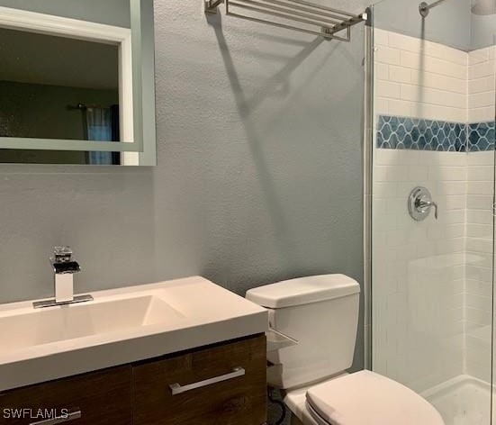 bathroom with vanity, a tile shower, and toilet