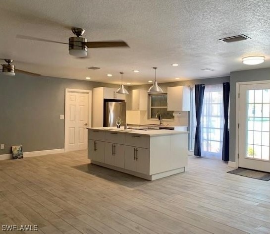 kitchen with stainless steel fridge, a kitchen island with sink, decorative light fixtures, and white cabinets