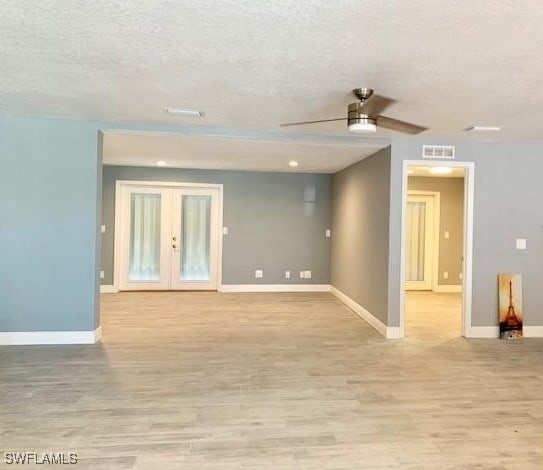 empty room with french doors, a textured ceiling, light hardwood / wood-style floors, and ceiling fan