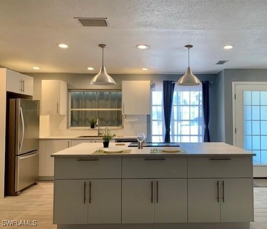 kitchen featuring stainless steel fridge, sink, hanging light fixtures, and gray cabinetry