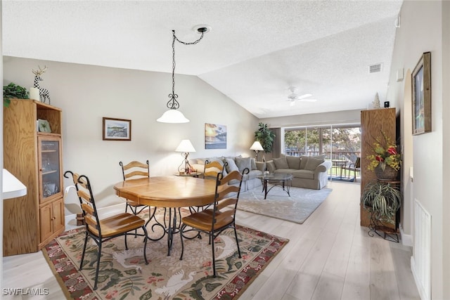 dining space featuring vaulted ceiling, a textured ceiling, light wood-type flooring, and ceiling fan