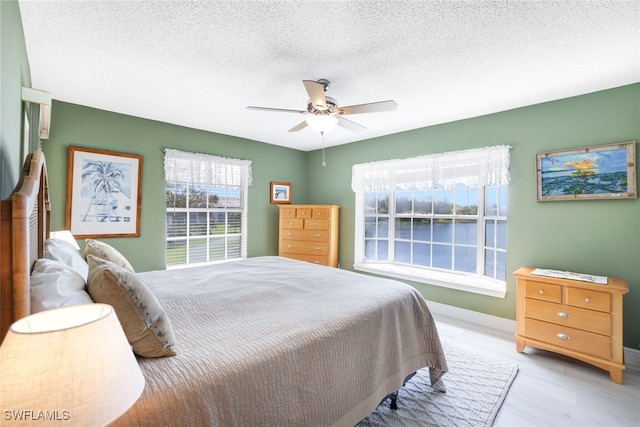 bedroom with ceiling fan, a textured ceiling, and light hardwood / wood-style flooring