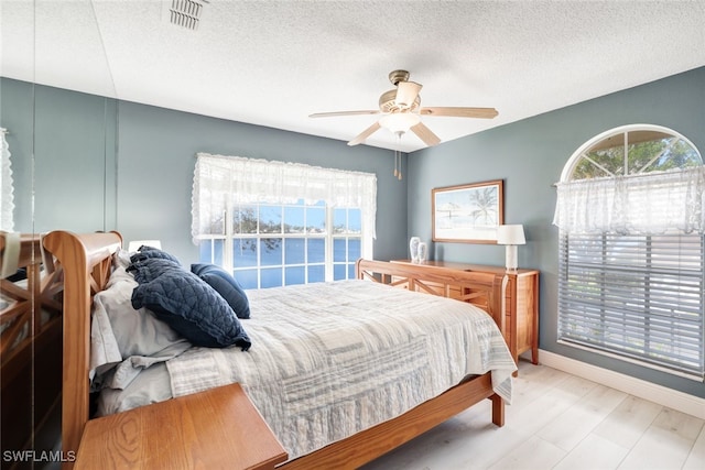 bedroom with a textured ceiling, light wood-type flooring, and ceiling fan