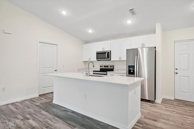 kitchen with white cabinets, an island with sink, sink, appliances with stainless steel finishes, and vaulted ceiling