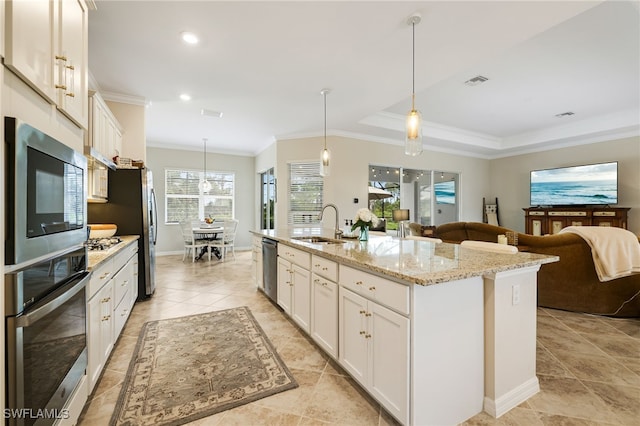 kitchen featuring appliances with stainless steel finishes, ornamental molding, a center island with sink, white cabinets, and hanging light fixtures