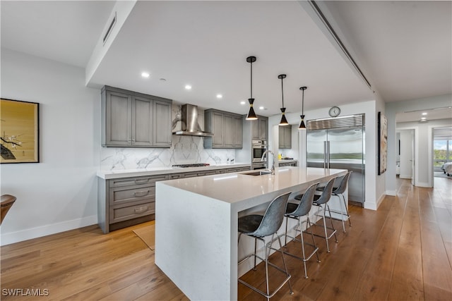 kitchen with appliances with stainless steel finishes, wall chimney exhaust hood, light hardwood / wood-style flooring, and a breakfast bar