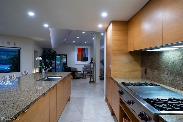 kitchen featuring dark stone counters, sink, vaulted ceiling, stainless steel gas range oven, and backsplash