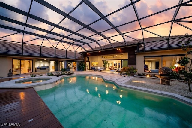 pool at dusk featuring an in ground hot tub, a lanai, and a patio area