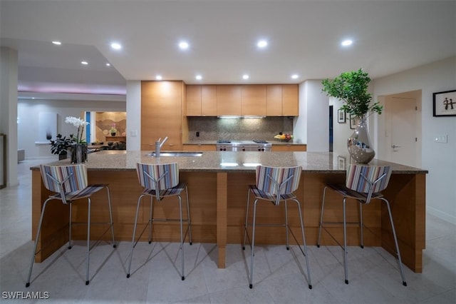 kitchen featuring light stone counters, sink, backsplash, a breakfast bar, and stainless steel range