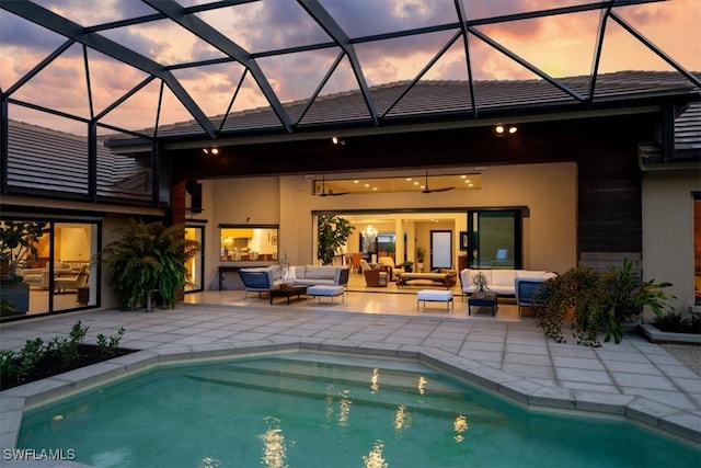 pool at dusk featuring an outdoor living space, glass enclosure, and a patio