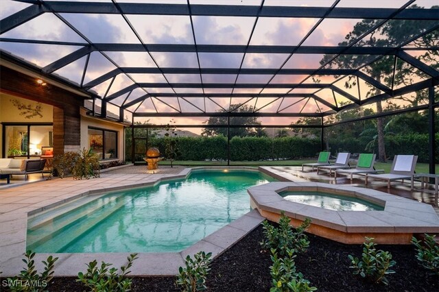 pool at dusk featuring glass enclosure, an in ground hot tub, and a patio area