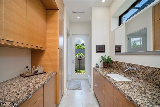 kitchen featuring a healthy amount of sunlight, stone counters, sink, and light tile patterned floors