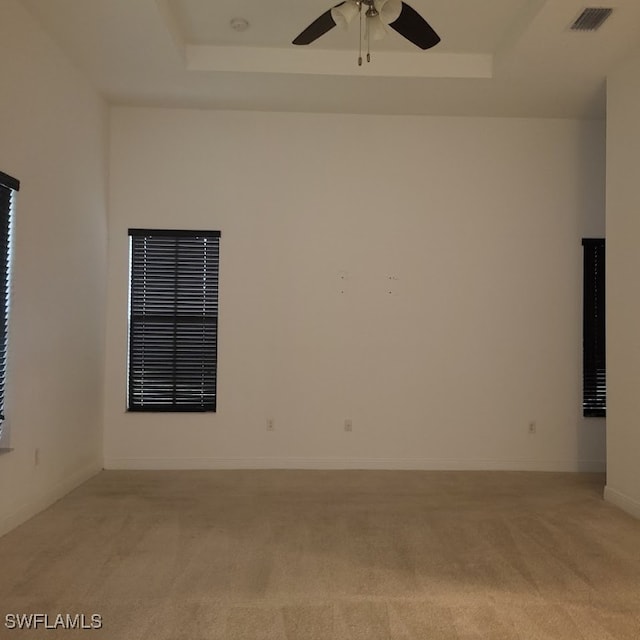 spare room with a tray ceiling, ceiling fan, and light colored carpet