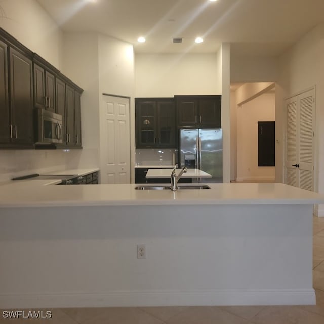 kitchen featuring dark brown cabinets, light tile patterned flooring, sink, kitchen peninsula, and appliances with stainless steel finishes