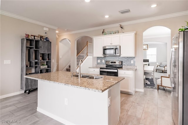 kitchen with light stone counters, white cabinets, stainless steel appliances, a kitchen island with sink, and sink