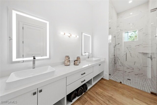 full bath with double vanity, a marble finish shower, a sink, and wood finished floors