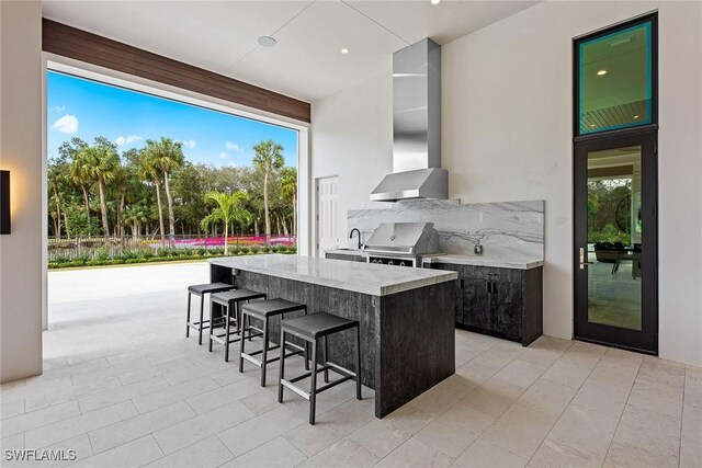 kitchen with a kitchen island, a kitchen breakfast bar, wall chimney range hood, light stone countertops, and modern cabinets