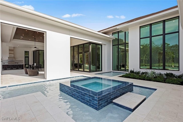 view of pool featuring a ceiling fan, a pool with connected hot tub, a patio, and exterior kitchen