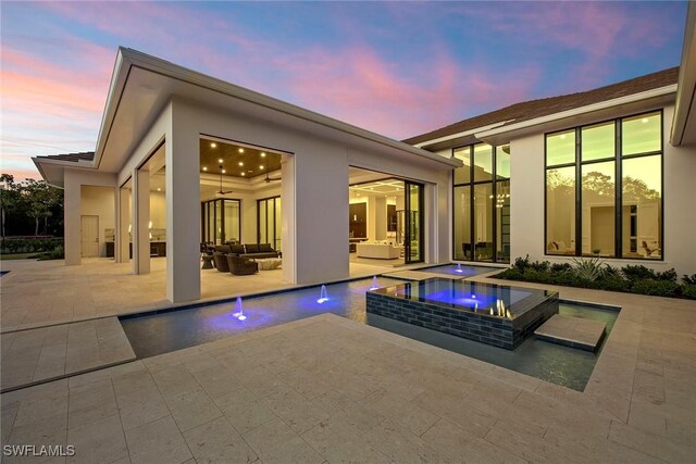 rear view of house with a patio area, stucco siding, a ceiling fan, and an in ground hot tub