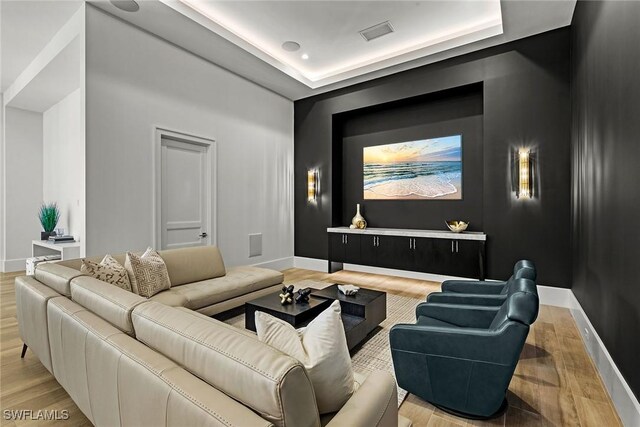 home theater featuring baseboards, visible vents, a raised ceiling, and wood finished floors