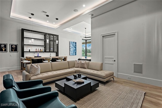 living room with visible vents, wet bar, a tray ceiling, and wood finished floors