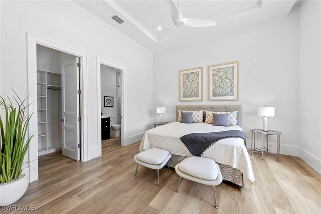 bedroom featuring baseboards, visible vents, light wood-style flooring, a tray ceiling, and a walk in closet