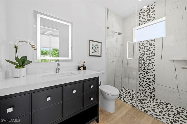 bathroom with vanity, tiled shower, wood finished floors, and toilet